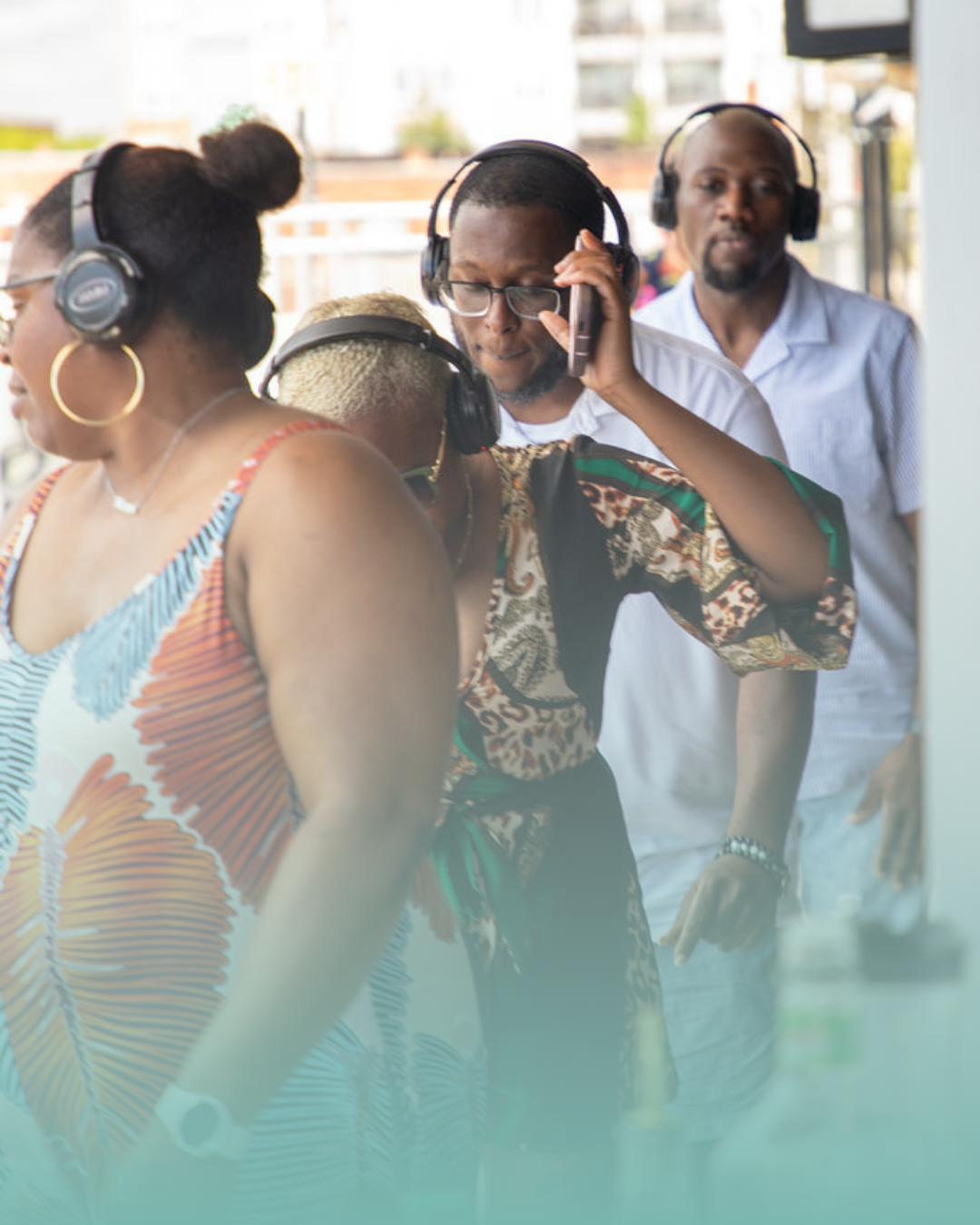 A group of people enjoying an outdoor daytime party, wearing black wireless headphones for a silent disco and dancing near a bar setup.